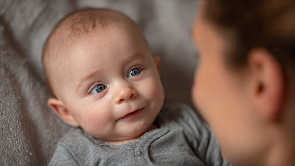 4 Month Olds And Early Autism Signs A Guide For Caregivers A 4-month-old baby lying on a soft surface making eye contact with a caregiver, highlighting early interaction and development